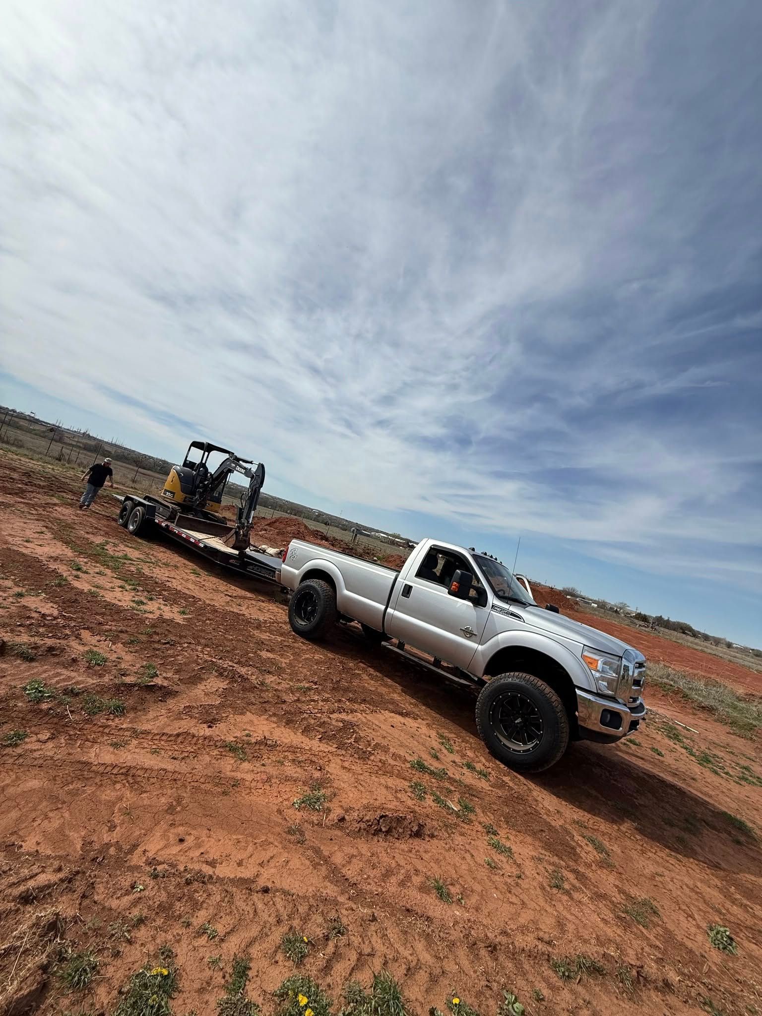 A white truck is driving down a dirt road with a trailer attached to it.