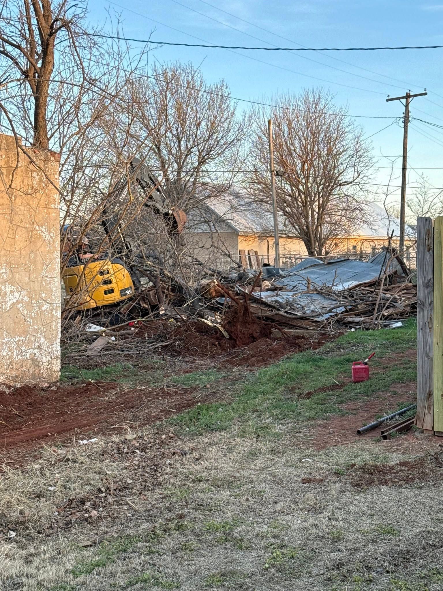 A yellow excavator is demolishing a building in a yard.