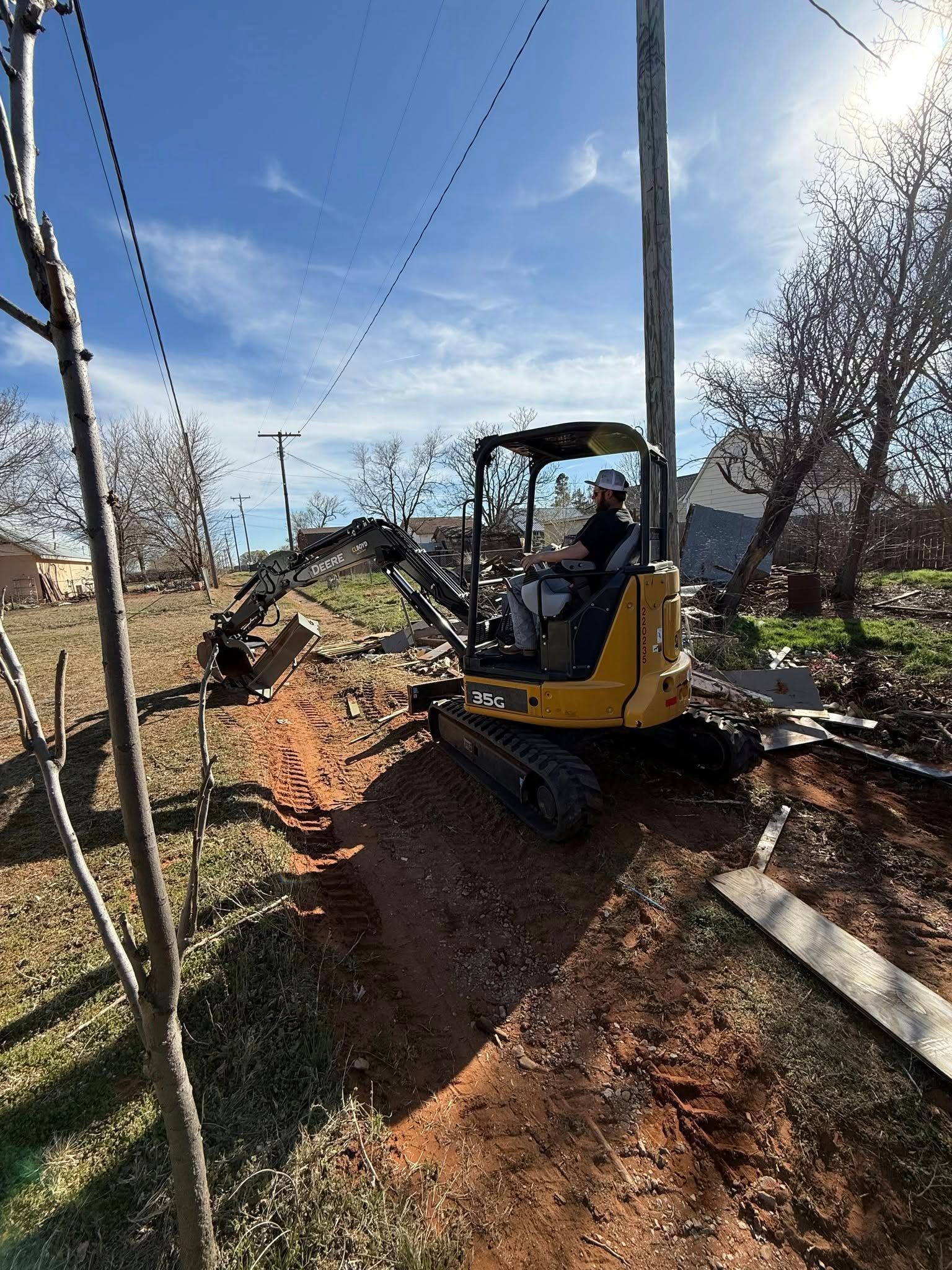 A man is driving a yellow excavator in a dirt field.