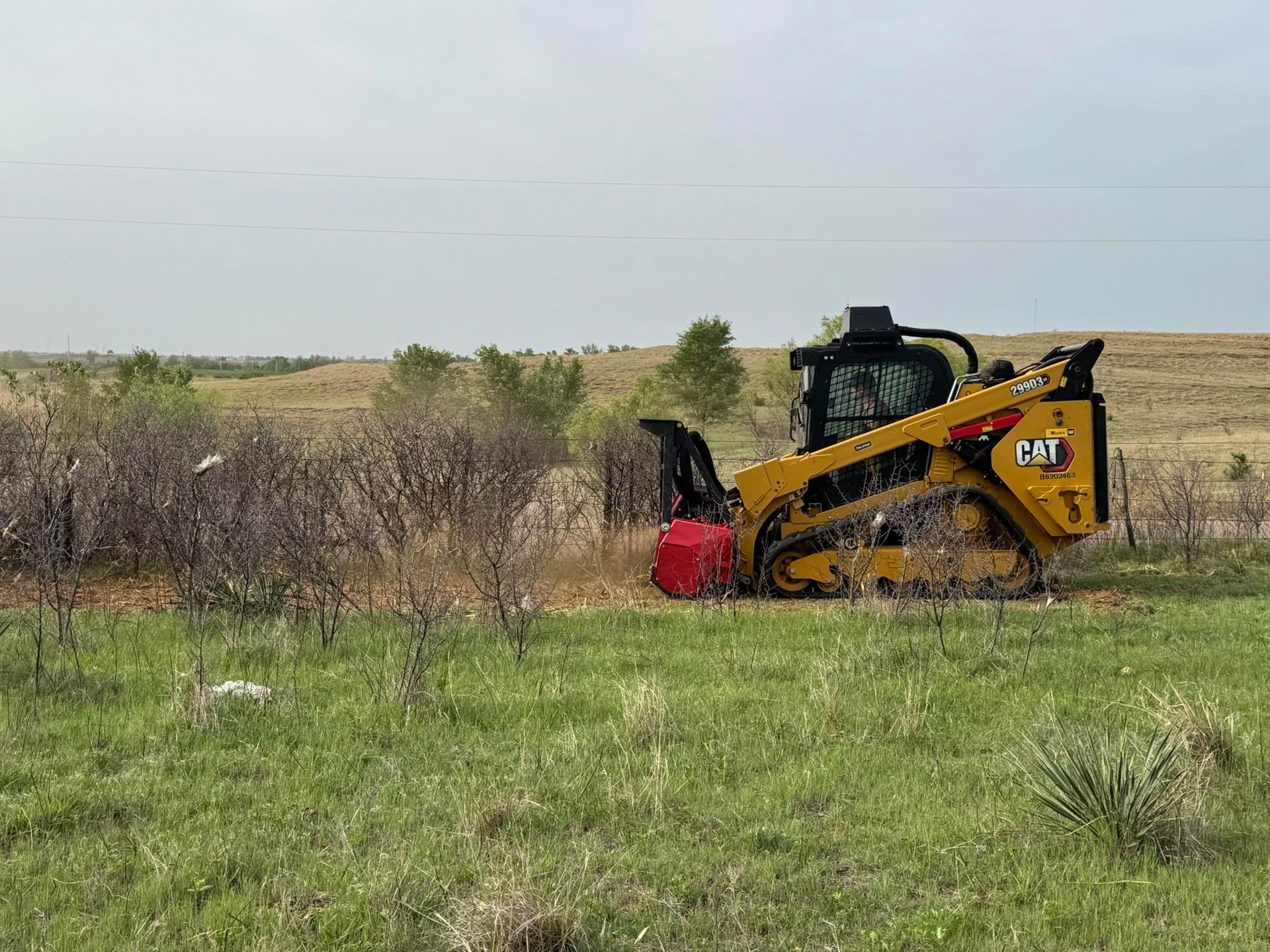 A bulldozer is cutting brush in a grassy field.