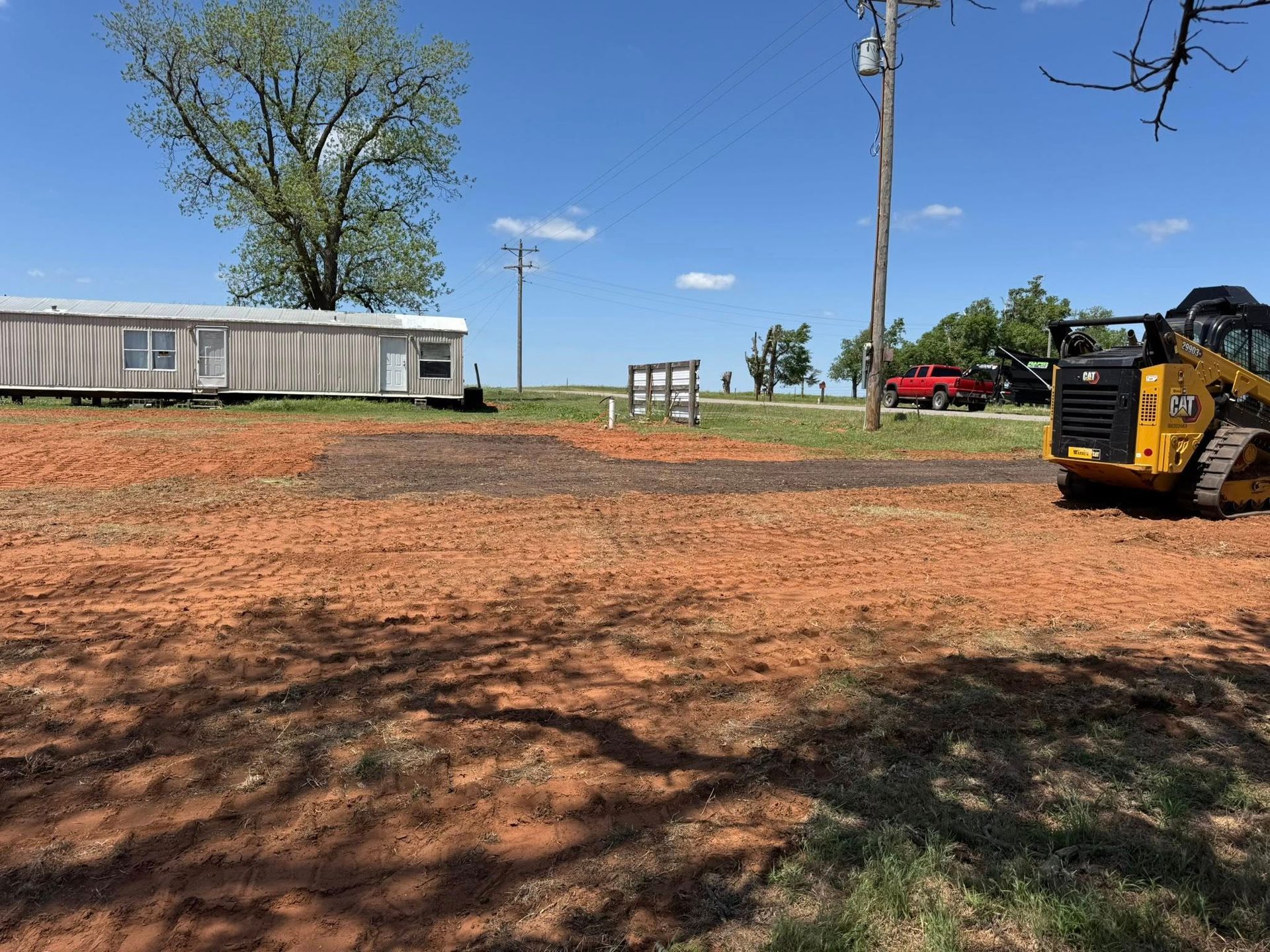A bulldozer is moving dirt in a field next to a mobile home.