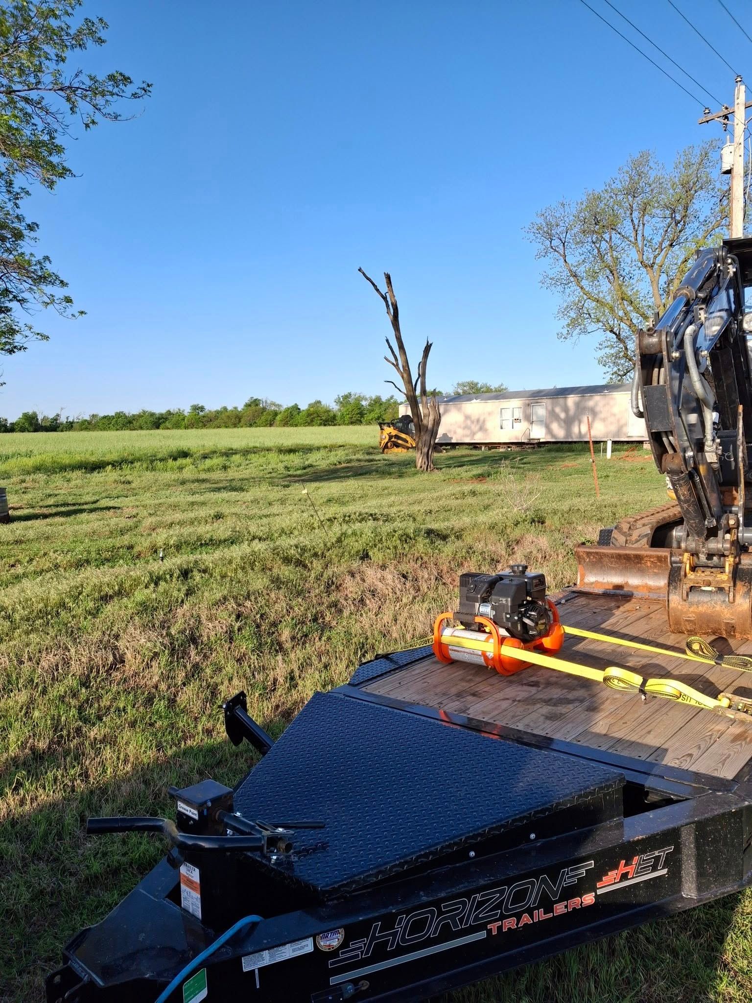 A trailer with a machine on it is parked in a grassy field.