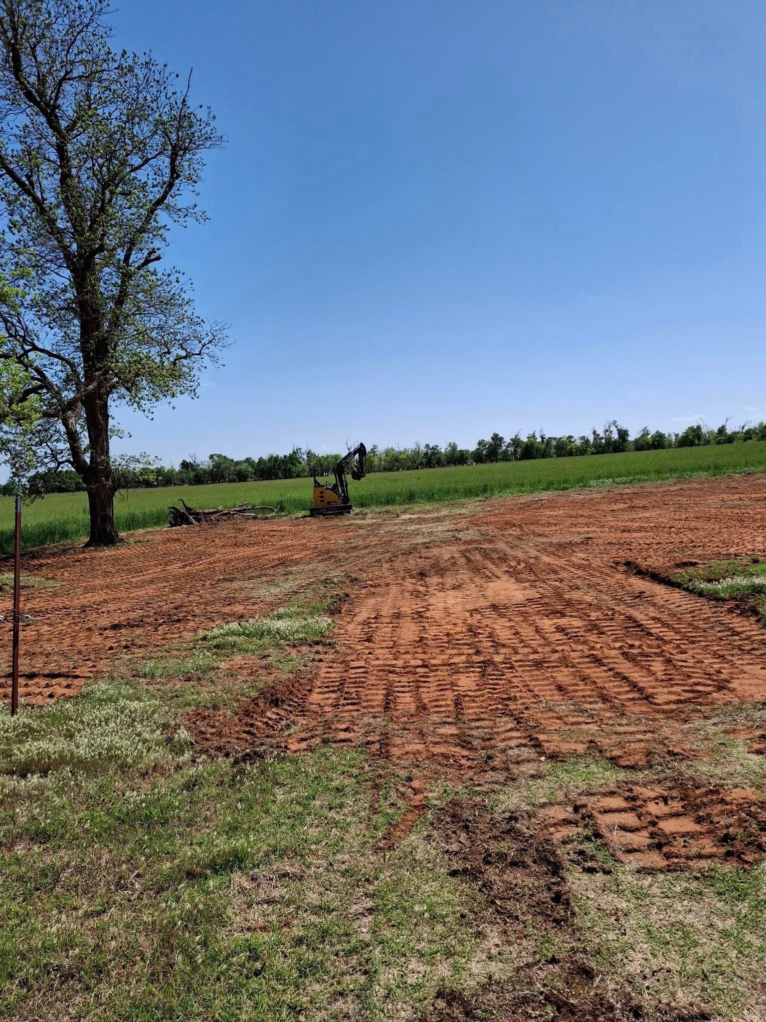 A large dirt field with a tree in the middle and a bulldozer in the background.