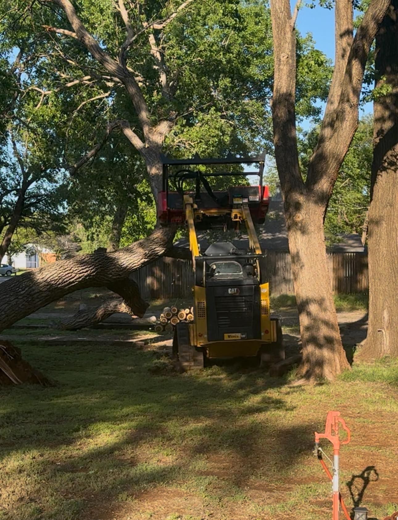 A yellow tractor is cutting a tree in a yard.