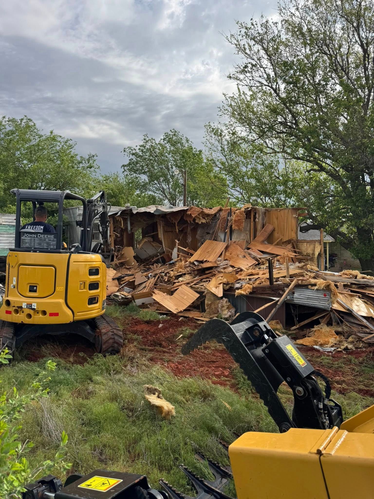 A yellow excavator is demolishing a house in a field.