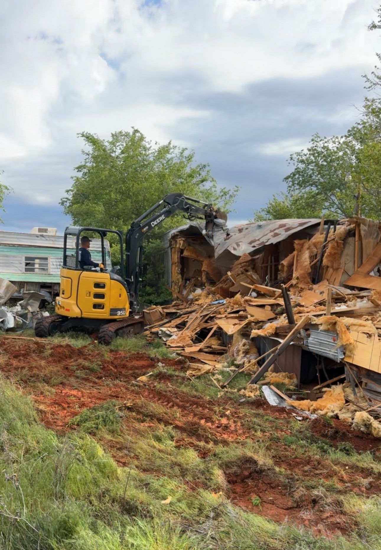 A yellow excavator is demolishing a house in a field.