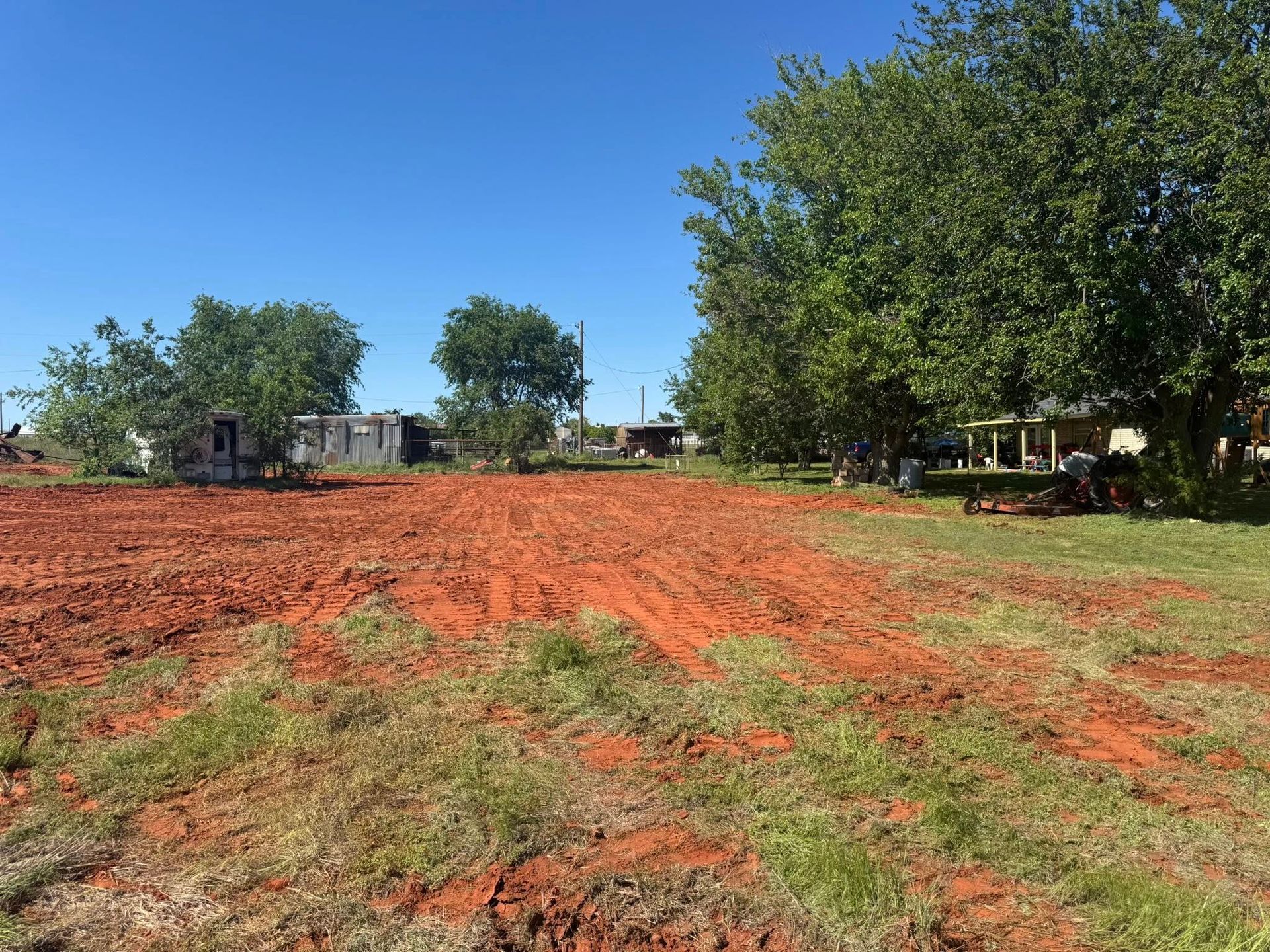 A dirt field with a house in the background and trees in the foreground.