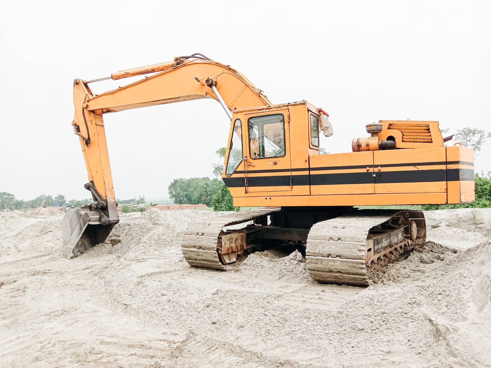 A man is driving a deere excavator in a dirt field.
