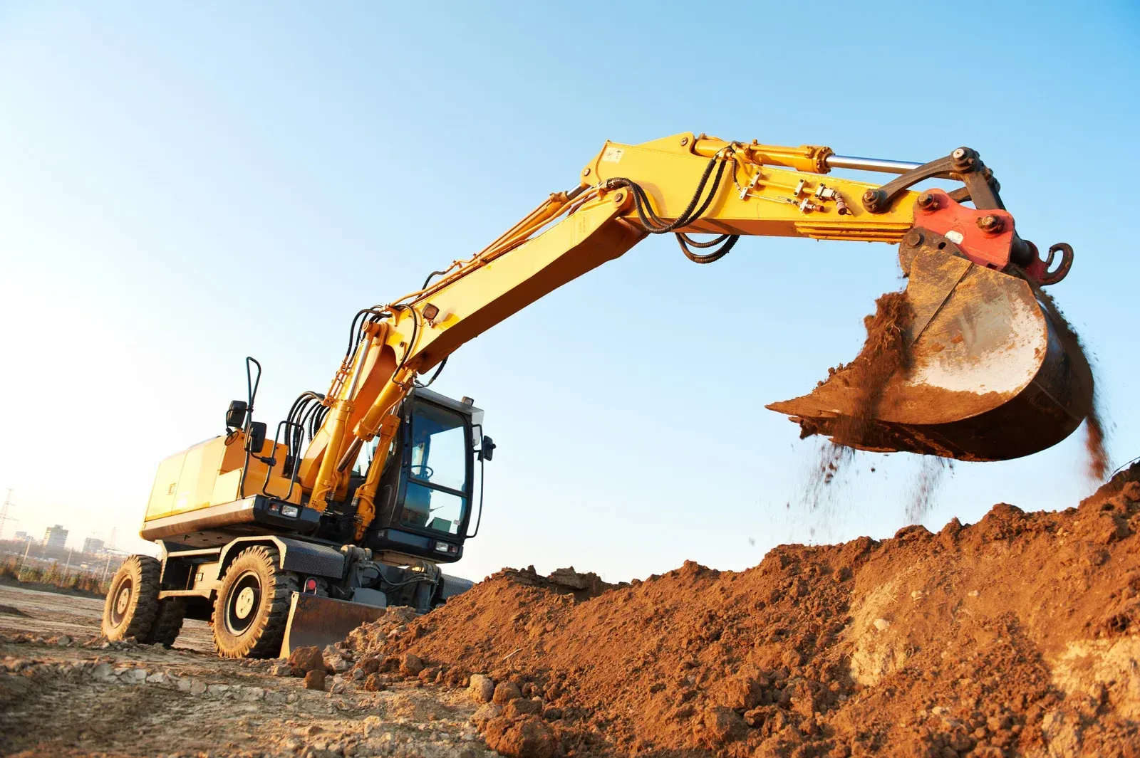 A yellow excavator is digging in a dirt field next to a bulldozer.