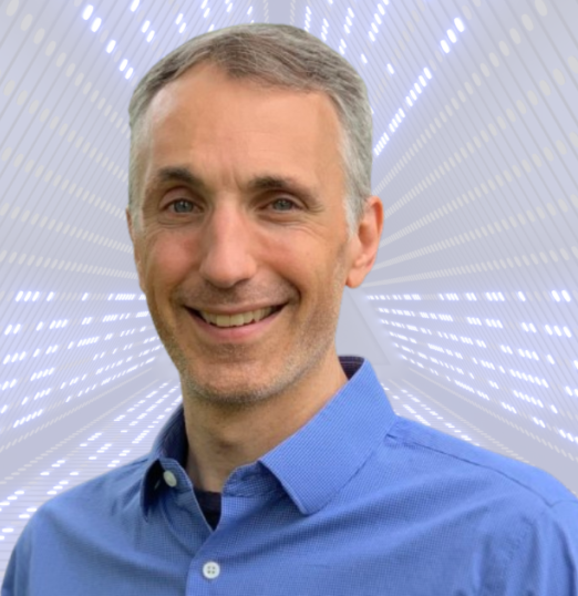 A woman is sitting at a desk with her hands folded and smiling.