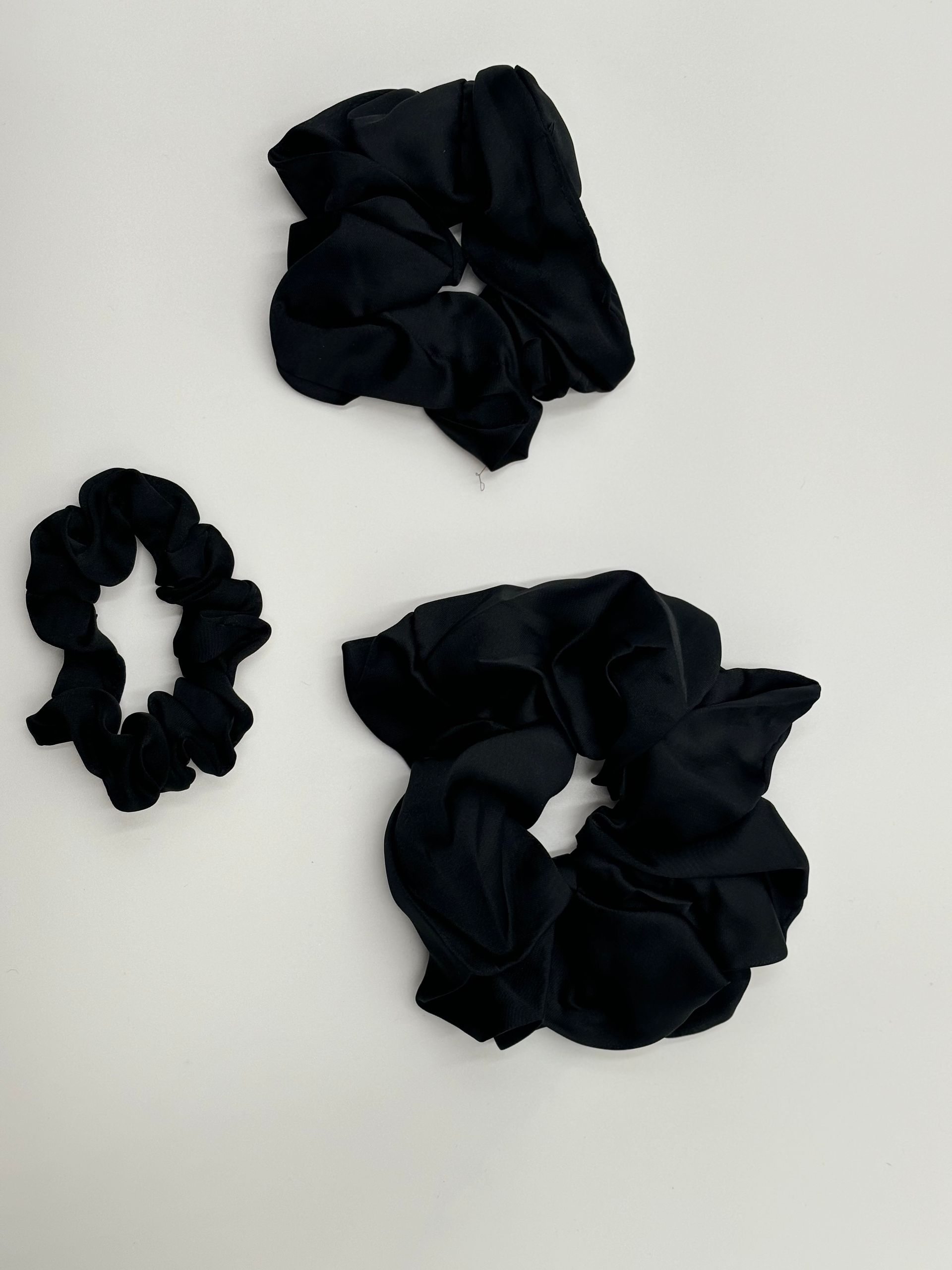 Three satin scrunchies in different sizes  in color ebony, laid out side by side in Crown Color System shades