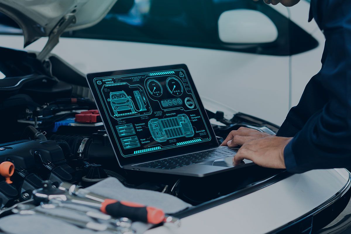 Mechanic using a laptop to diagnose a car engine. The screen displays diagnostic data.