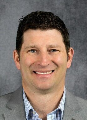 A man in a suit and plaid shirt is smiling for the camera.