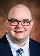 A bald man wearing glasses and a suit and tie is smiling for the camera.