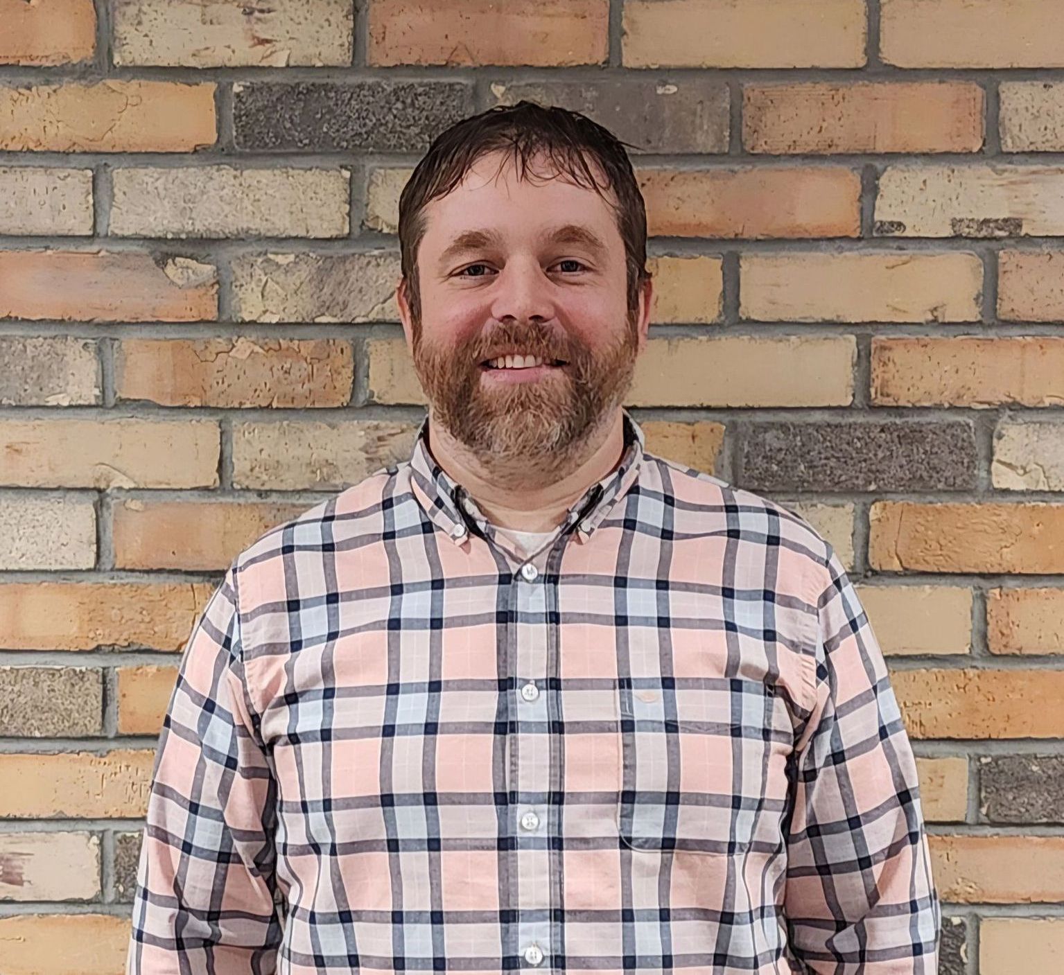 A man in a plaid shirt is standing in front of a brick wall.