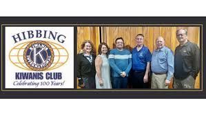 A group of people standing next to each other in front of a kiwanis club logo.