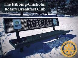 A park bench in the snow with the words `` the hibbing-chisholm rotary breakfast club '' written on it.