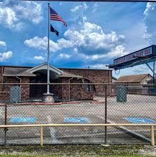 An american flag is flying in front of a brick building behind a chain link fence.