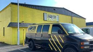 A black van is parked in front of a yellow building.