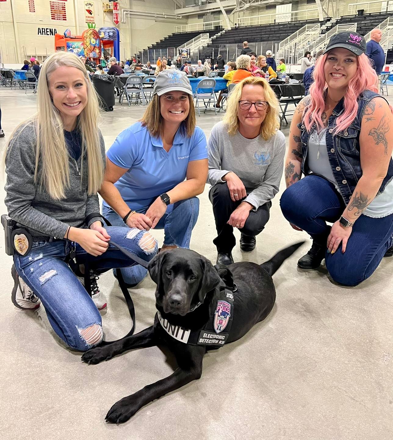 A group of women are posing for a picture with a black dog.