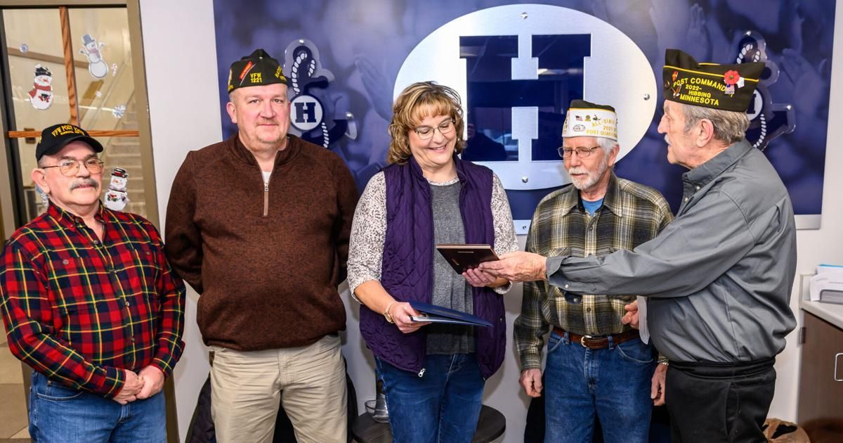 A group of people are standing next to each other in front of a wall with a letter h on it.