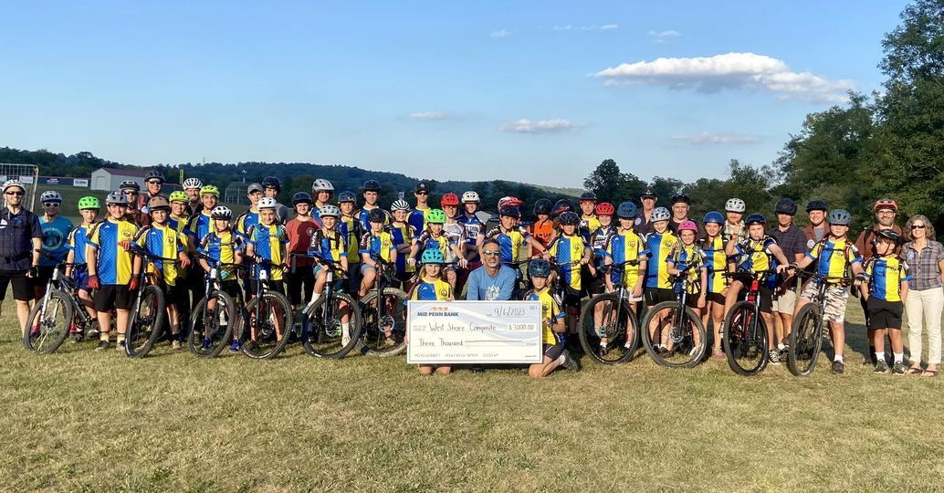 A large group of people are standing in a field with bicycles.