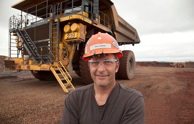 A man wearing a hard hat is standing in front of a dump truck