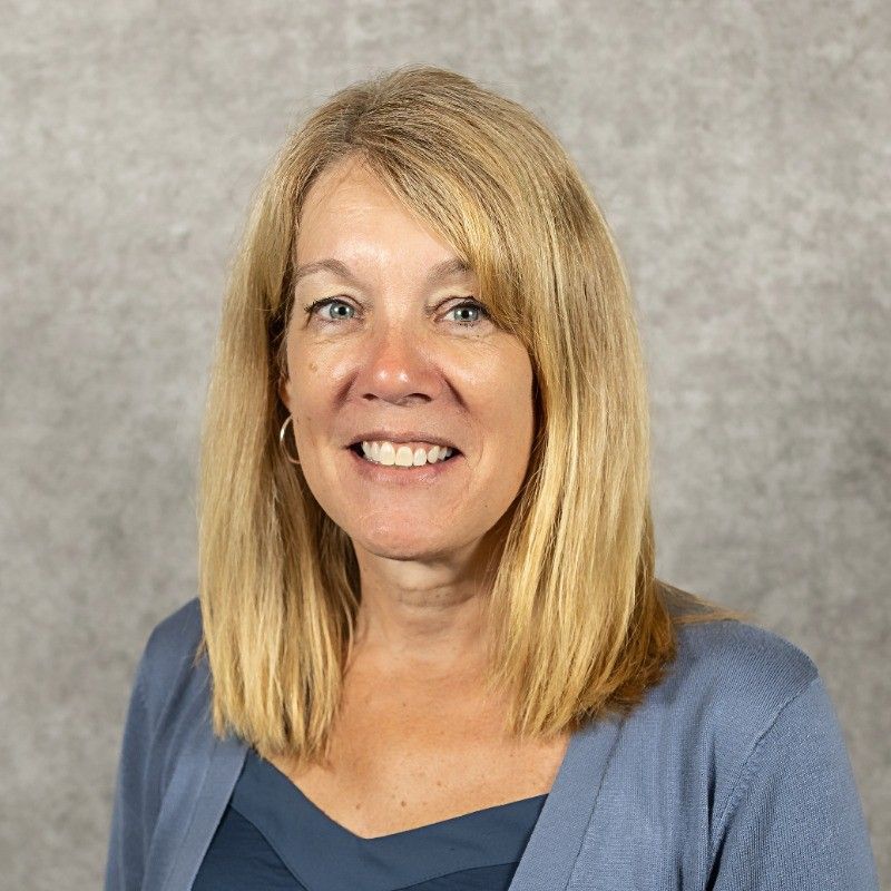 A woman with blonde hair is wearing a blue sweater and smiling.