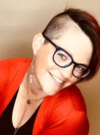 A woman wearing glasses and a red sweater is smiling.