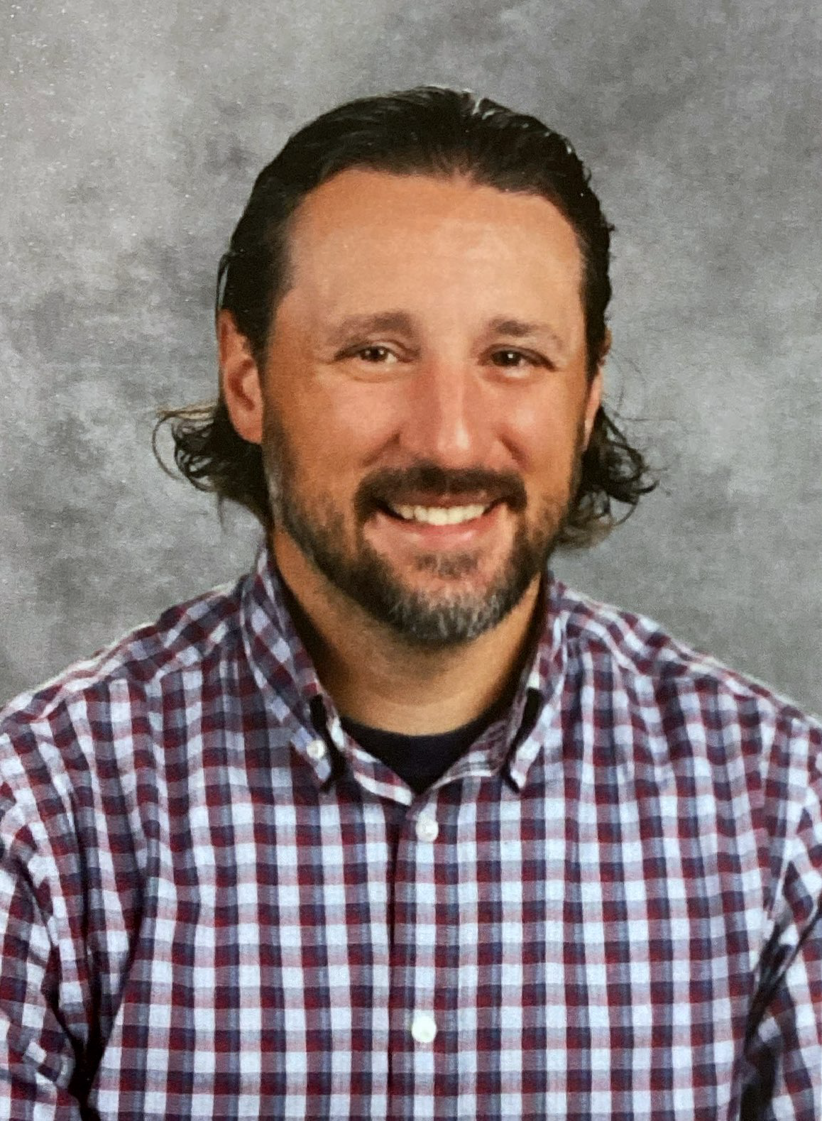 A bald man with a beard and glasses is smiling in front of a brick wall.