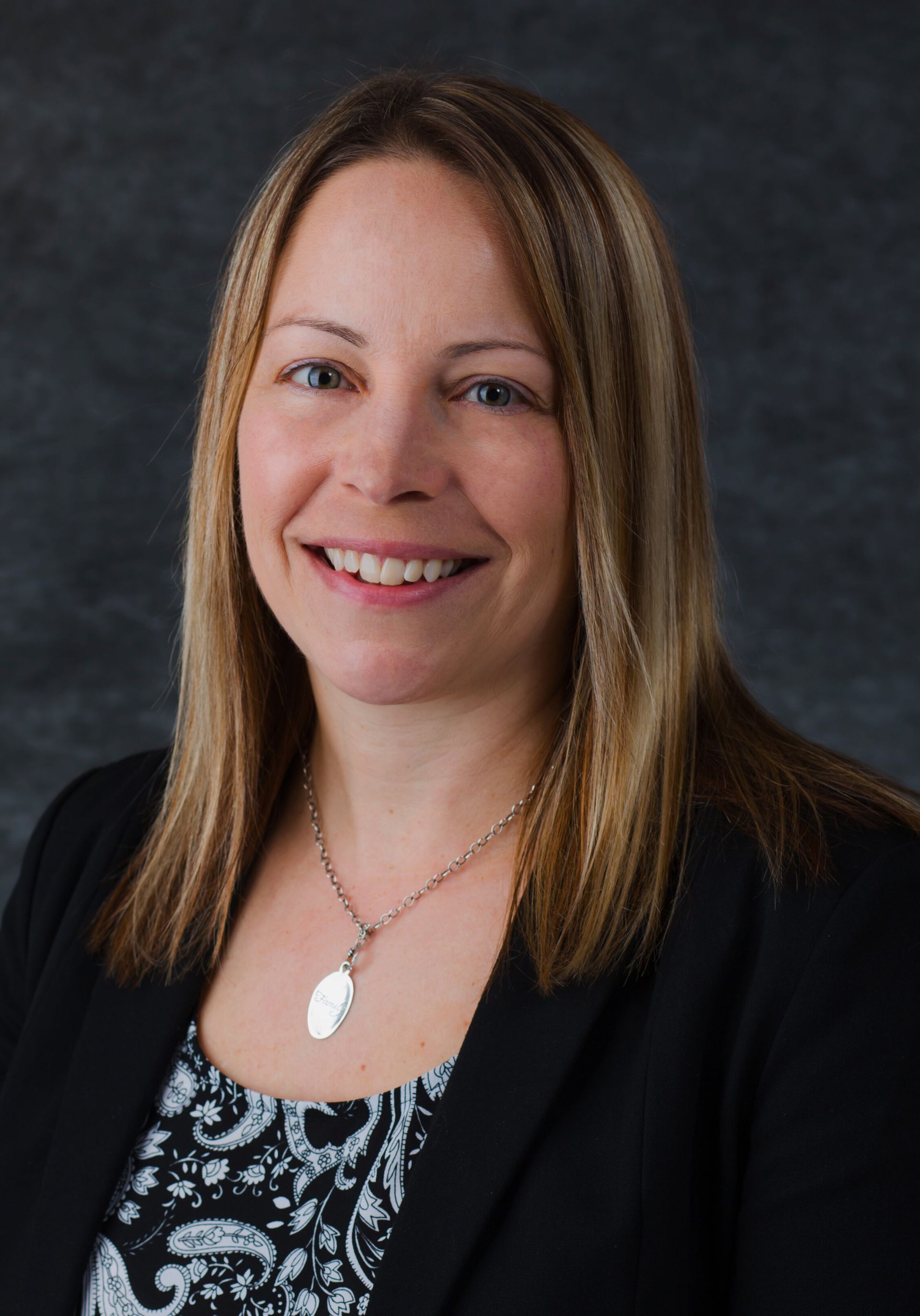 A woman wearing a black jacket and a necklace is smiling for the camera.