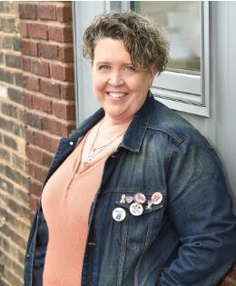 A woman in a denim jacket is leaning against a brick wall.