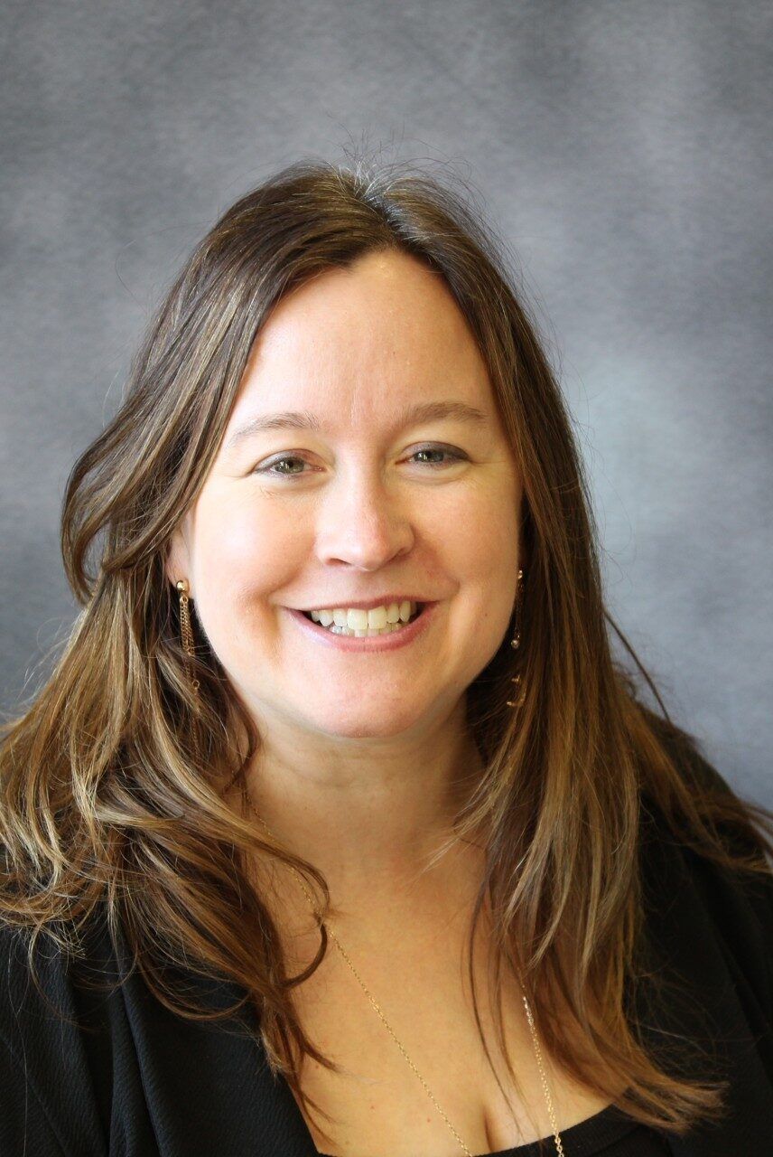 A woman with long brown hair is smiling for the camera.