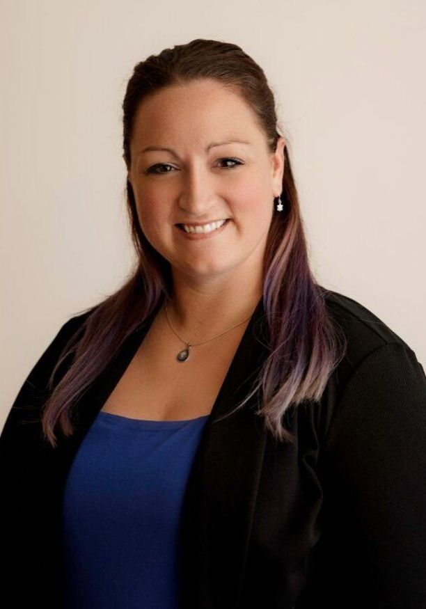 A woman with purple hair is wearing a blue shirt and a black jacket.