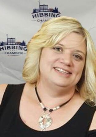 A woman wearing a black shirt and a necklace is smiling.