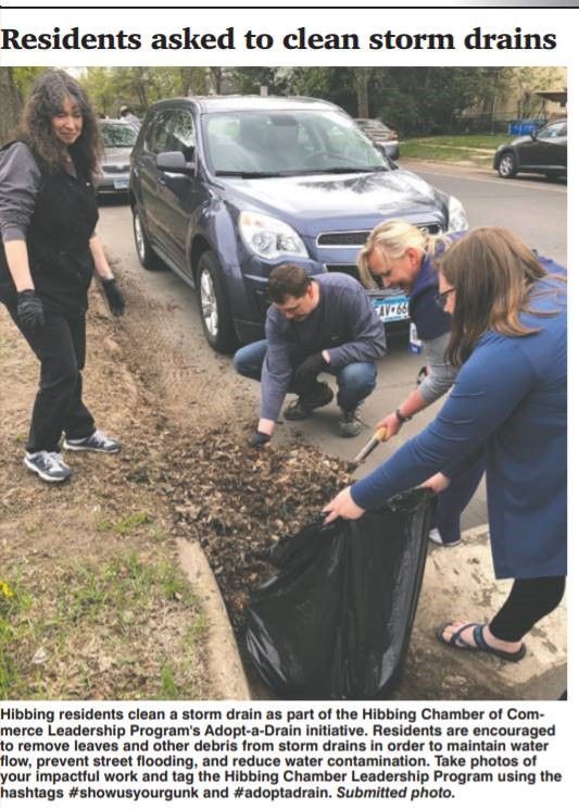 A group of people are cleaning storm drains in front of a car.