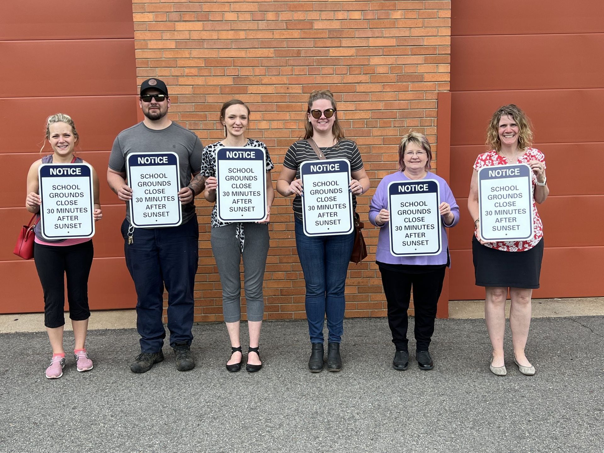 A group of people are standing in front of a brick wall holding signs.