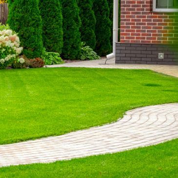 A brick walkway leading to a lush green lawn in front of a brick house.