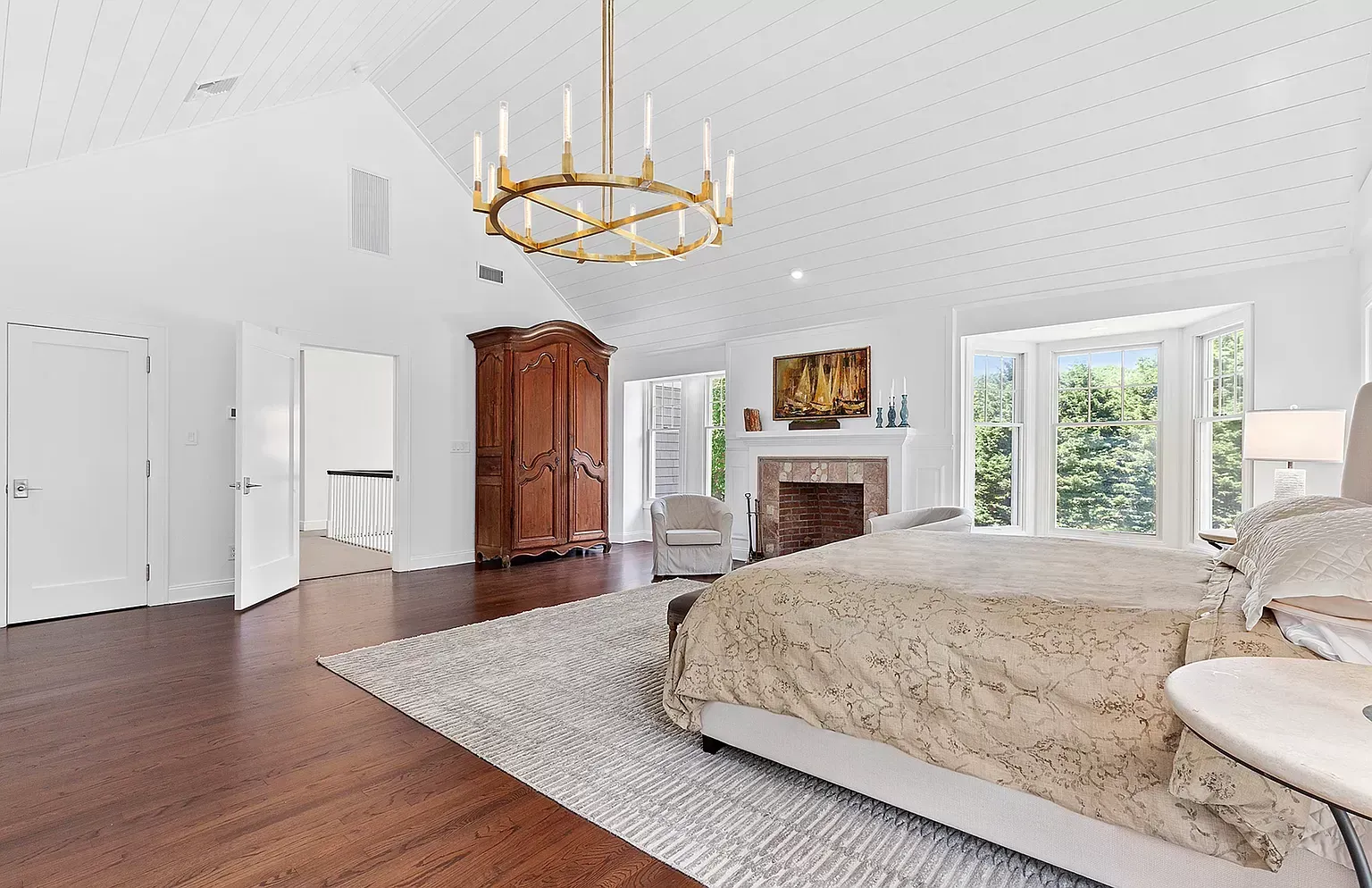 A bedroom with a large bed , fireplace , rug and chandelier.