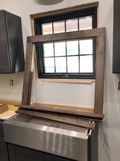 A wooden window frame is sitting on top of a stainless steel sink in a kitchen.