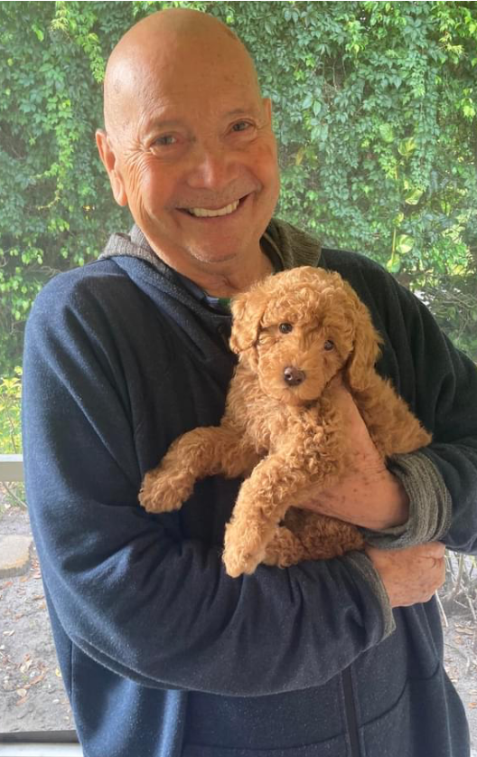 A bald man is holding a brown puppy in his arms.