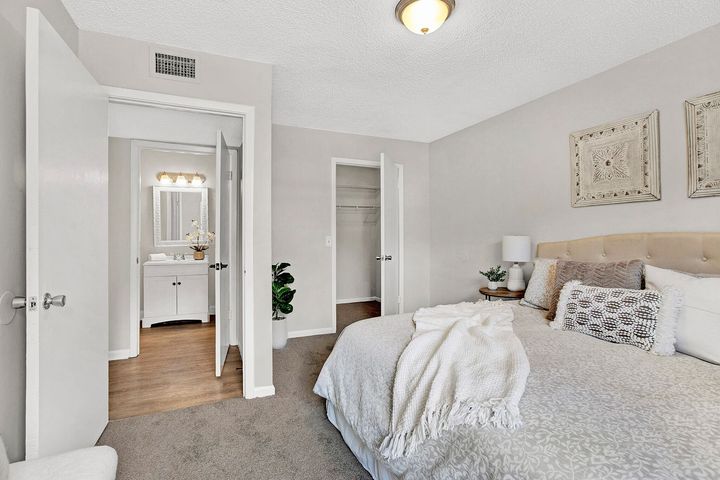 Bedroom with bed, bathroom door open, closet, neutral colors, decor.