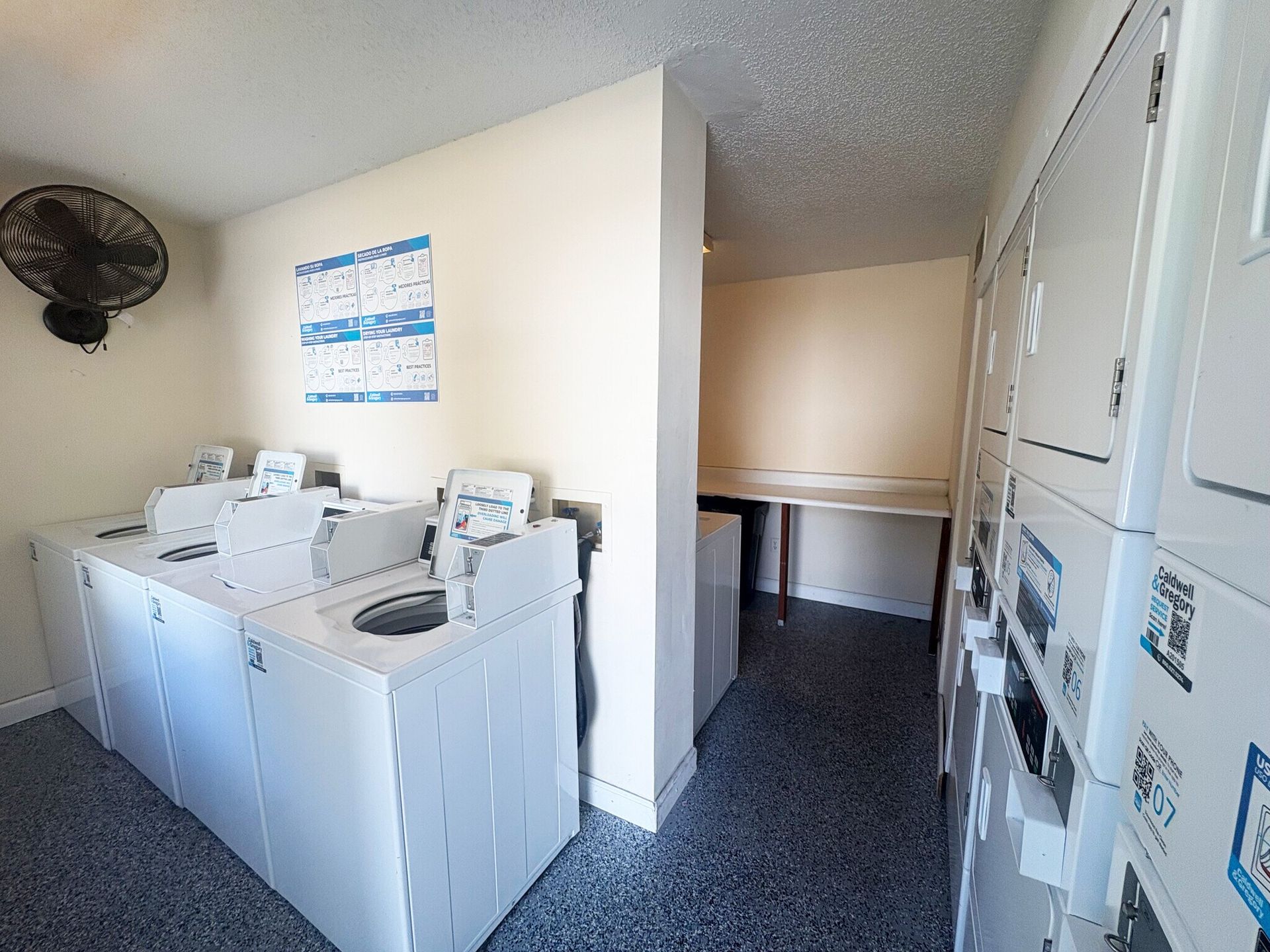 Laundry room with washing machines, dryers, and lockers. A fan is mounted on the wall.