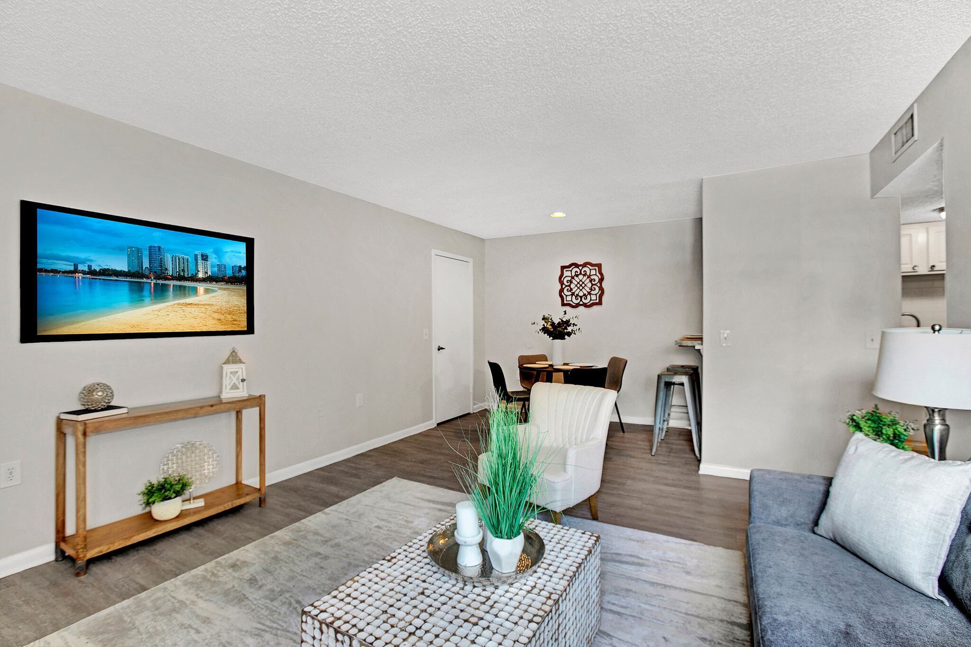 Living room with TV, sofa, and dining area. Gray walls, wood flooring, neutral furniture.
