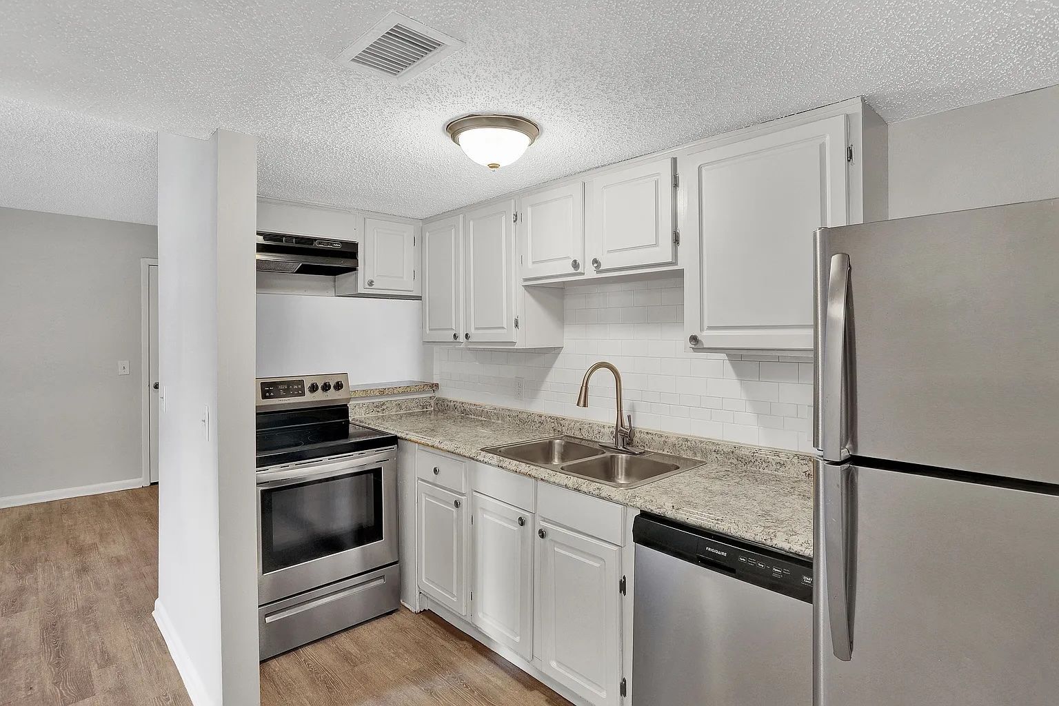 A small kitchen with white cabinets, stainless steel appliances, and a light speckled countertop.