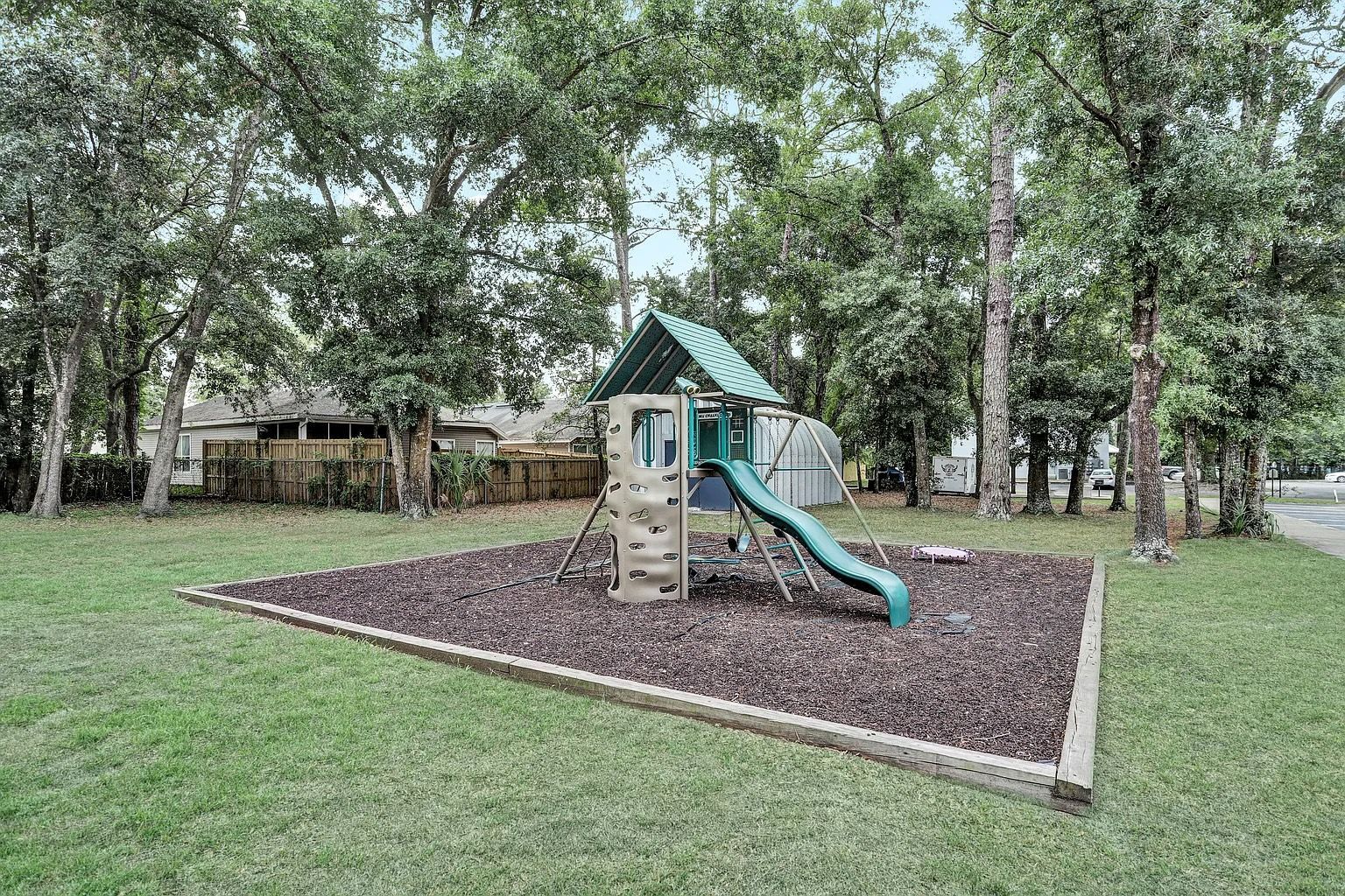 Playground set on wood chips in grassy area, surrounded by trees.