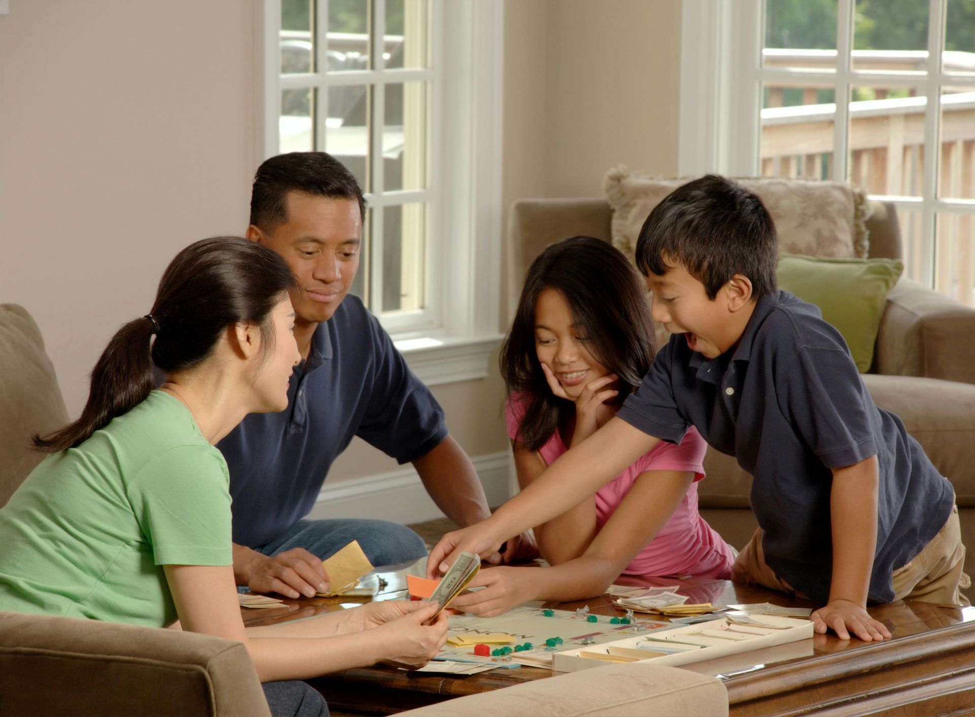 Family gathered around a board game on a table in a living room; smiling, interacting.