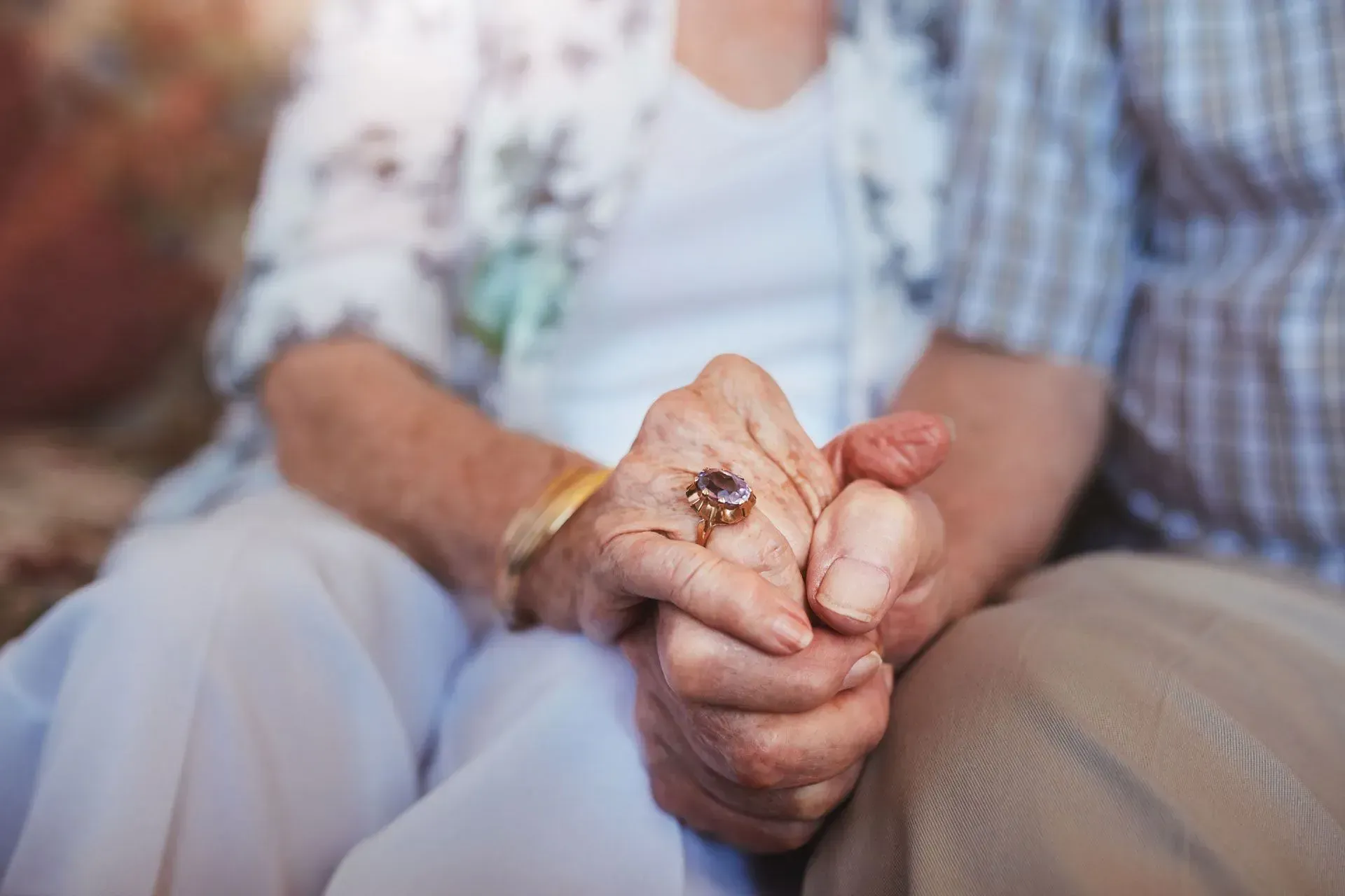 An elderly couple is holding hands while sitting on a couch.