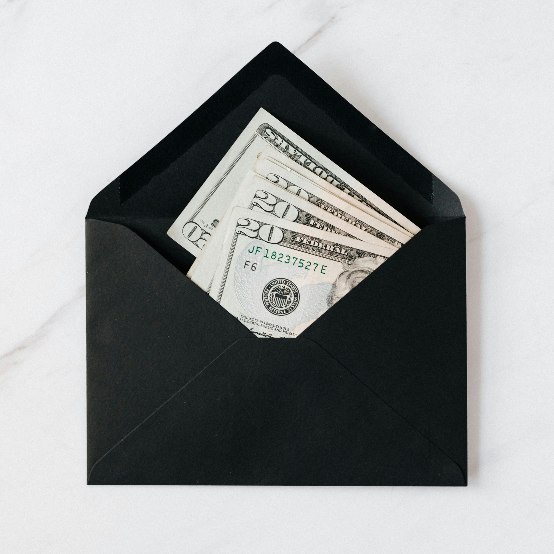 Black envelope partially open, holding several US $20 bills, on a white surface.