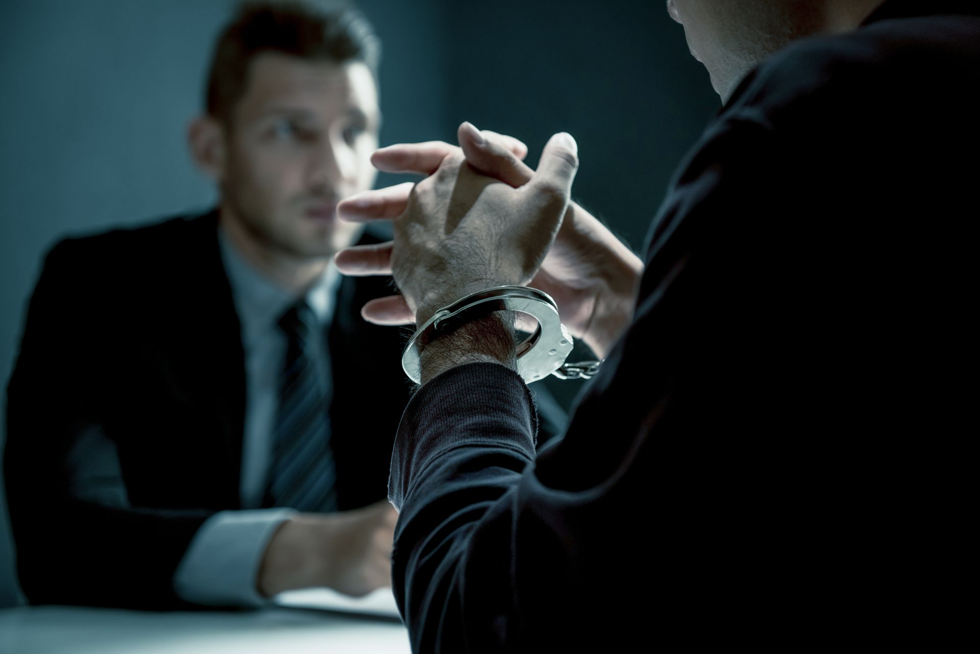 a man in handcuffs is sitting at a table talking to a man in a suit .